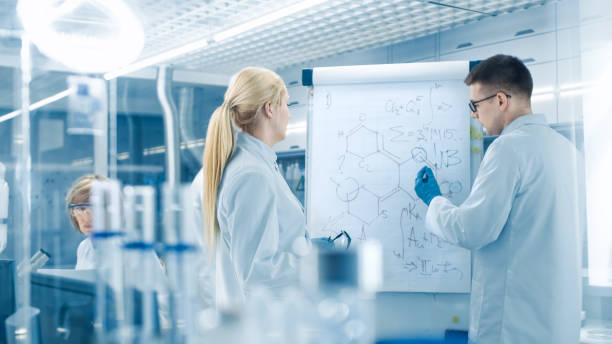Young Female and Male Scientists Write Formulas on a Whiteboard. They're Solving Scientific Problems in Bright Modern High Tech Laboratory. Young Female and Male Scientists Write Formulas on a Whiteboard. They're Solving Scientific Problems in Bright Modern High Tech Laboratory. chemical formula stock pictures, royalty-free photos & images