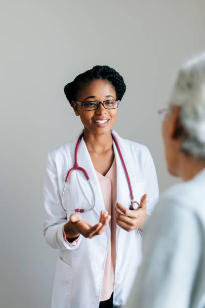 Young female doctor explaining senior patient A young female doctor wearing a lab coat, explaining to a senior patient, looking at each other and smiling. beautiful haitian women stock pictures, royalty-free photos & images