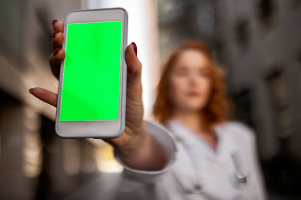 Young female doctor holding smartphone with green background Young female doctor holding smartphone with green background smart phone green background stock pictures, royalty-free photos & images
