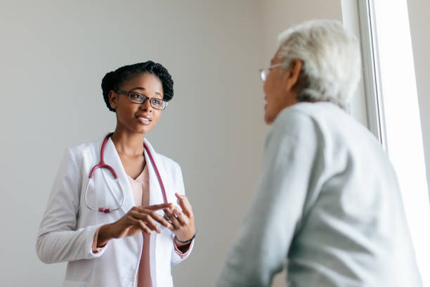 Young female doctor talking to female senior patient A pretty young female doctor standing face to face with a senior female patient, looking at her and explaining. beautiful haitian women stock pictures, royalty-free photos & images
