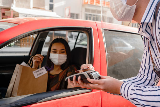 Young female driver receiving a packed coffee from a coffee shop Young female driver receiving a packed coffee from a coffee shop curbsidepickup stock pictures, royalty-free photos & images