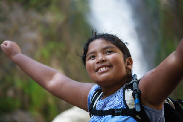 A young female hiker raising her arms into the air, accomplishment of a difficult hiking trail, with waterfall in the background. stock photo