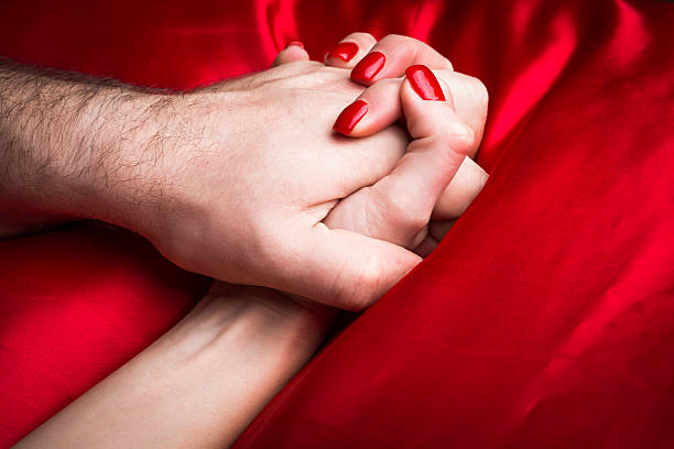 Young female holding hands sensually on red silk bed. stock photo