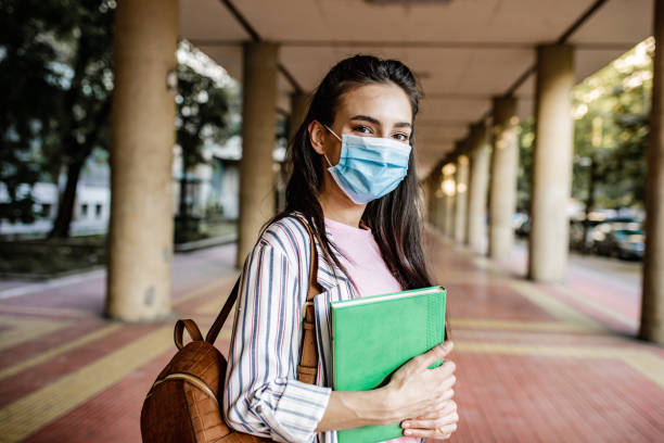 Young female student wearing protective face mask during pandemic A young woman is holding a notebook and wearing a face mask college student stock pictures, royalty-free photos & images