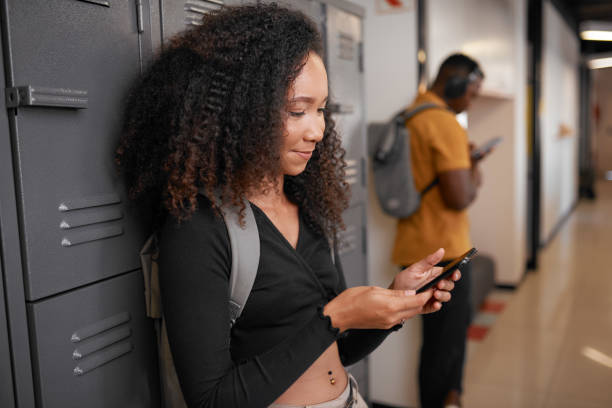 A young female student with a male on their phones in a college locker corridor stock photo