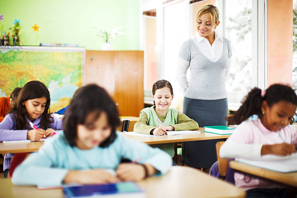 Young female teacher working with pupils in classroom. Young smiling female teacher working with the group of children in classroom. She is friendly looking.   students stock pictures, royalty-free photos & images