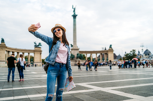 Young caucasian female tourist making selfies at town square in Budapest. Heroes Square/Hősök tere.