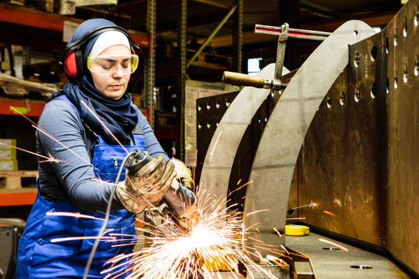 Young female trainee works with a grinder in a workshop, flying sparks stock photo