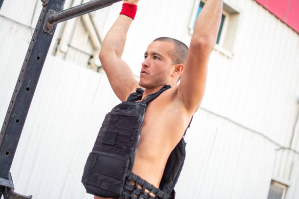Young fit man doing pull up exercise with a full of weight vest outdoors Young fit man doing pull up exercise with a full of weight vest outdoors waistcoat stock pictures, royalty-free photos & images