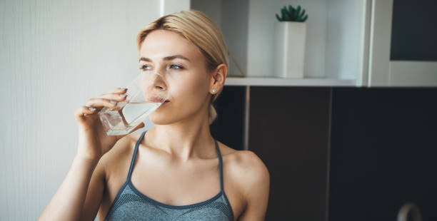 Young fitness lady drinking water after yoga exercises wearing sportswear at home in the kitchen stock photo