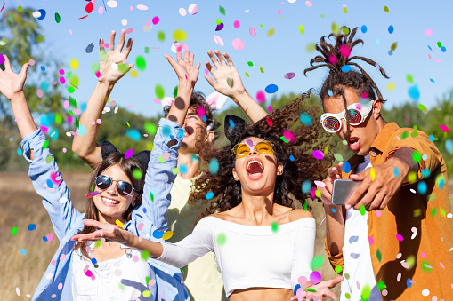 Happy excited friends having fun outdoor celebrating with confetti - Young millenial people enjoying summertime together at garden party - Cheerful friendship concept. Party - festival concept.