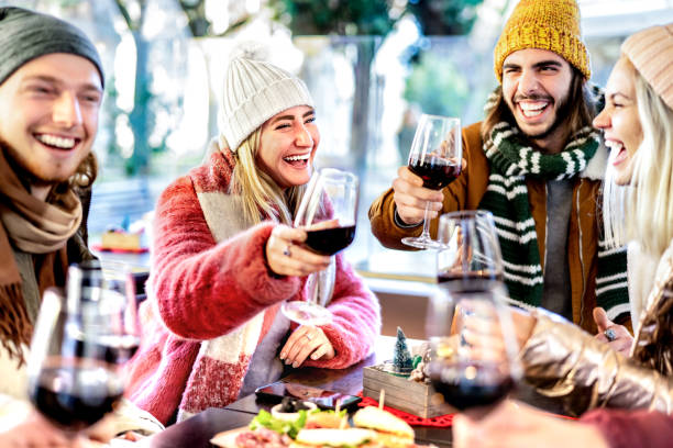 Young friends toasting red wine at restaurant patio - Happy people having fun together at winery bar wearing winter clothes - Dinning life style concept on bright filter with focus on left woman stock photo