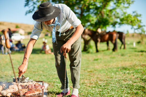 Young gaucho grilling meat in the traditional Argentinian way. Gaucho simple lifestyle scenes. Shot with a real family in Cordoba Argentina. argentina food stock pictures, royalty-free photos & images