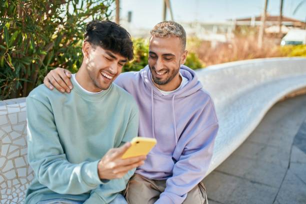 Young gay couple smiling happy using smartphone at the city. stock photo