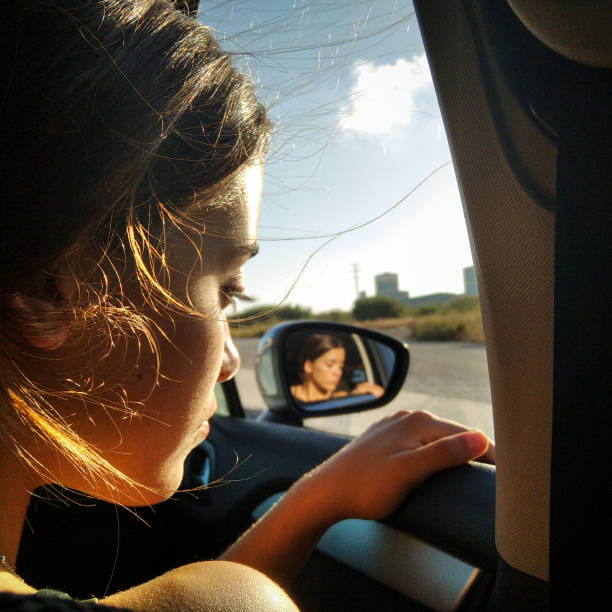 young  girl at the car window reflect in the rear view mirror, during a road trip stock photo