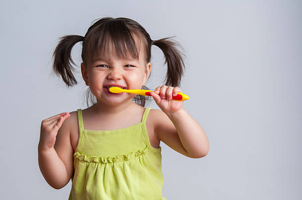 Young girl brushing teeth with yellow toothbrush stock photo