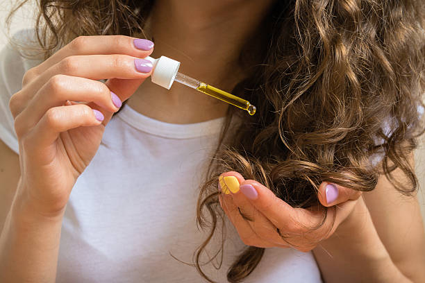 Young girl caring for curly hair tips with yellow oil stock photo