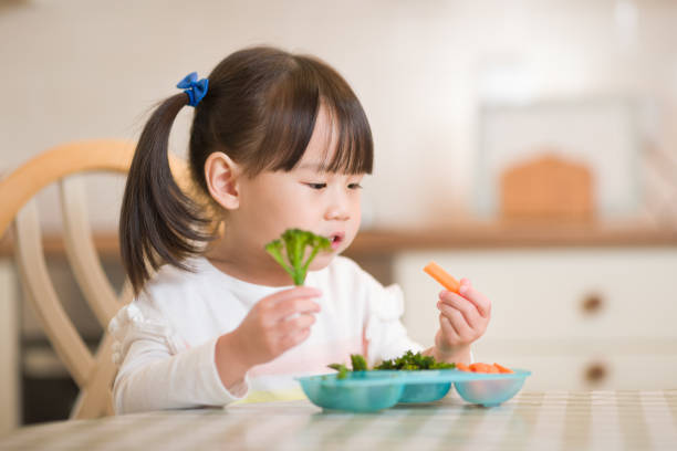 cô gái trẻ ăn rau xanh tươi trên nền nhà bếp thực sự - trẻ ăn rau hình ảnh sẵn có, bức ảnh & hình ảnh trả phí bản quyền một lần