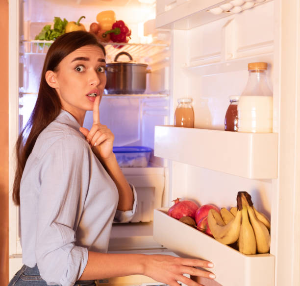 Young girl gesturing shh, taking cheat meal from refrigerator