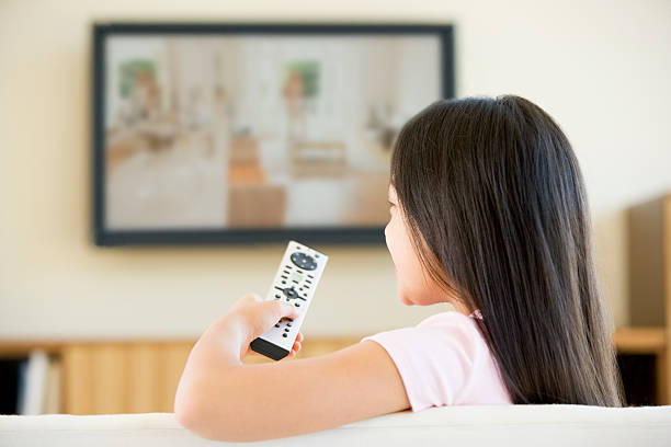 Young girl in living room with television and remote control Young girl in living room with flat screen television and remote control sitting on sofa watching TV asian kids watching tv stock pictures, royalty-free photos & images