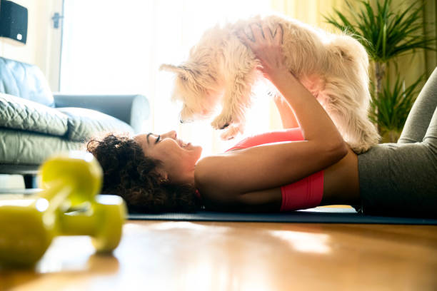Young girl in sportswear playing with her dog at home - Sporty woman training fitness workout indoor - Animals, sport and recreational concept stock photo