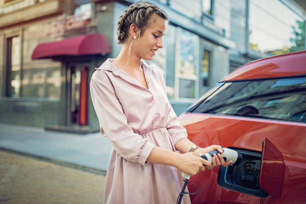 la joven está cargando su coche eléctrico en la ciudad - electric car fotografías e imágenes de stock