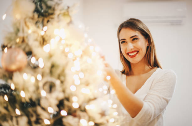 het jonge meisje bevestigt de lichten van kerstmis. - vrouw kerstboom versieren stockfoto's en -beelden
