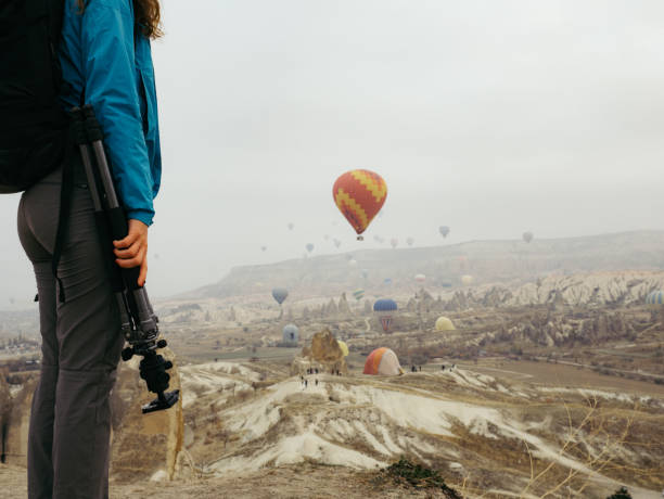 Young girl is  holding tripod while watching hot air balloons flying in red and rose valley in Goreme in Cappadocia in Turkey Cappadocia, Hot Air Balloon, Photographer, Famous Place, Turkey - Middle East hot middle eastern girls stock pictures, royalty-free photos & images
