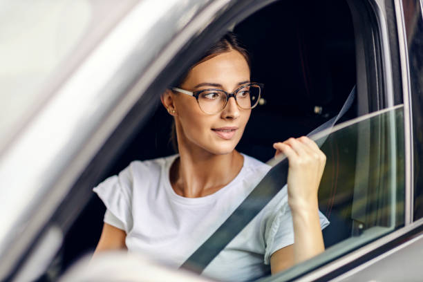 A young girl is sitting in her car and putting on the seat belt. She is just received her driving license. stock photo