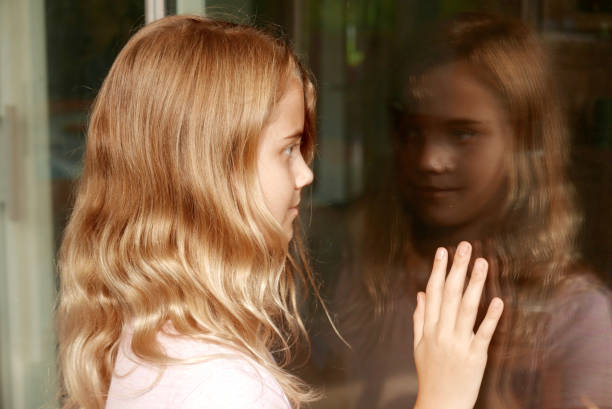 Young girl looking at her reflection in a window stock photo