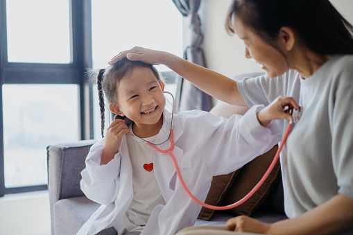 Image of an Asian young girl dressed up in doctor costume and playing a doctor with her grandmother
