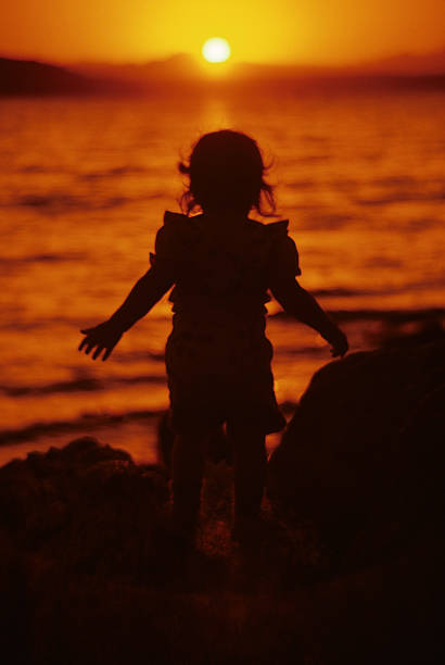 Young Girl Playing on the Beach at Sunset Puget Sound is a special body of water that belongs exclusively to Washington State. From the saltwater marshland of Olympia and Nisqually to the windy Strait of Juan de Fuca and the San Juan Islands, Puget Sound exhibits a quiet beauty that is quintessentially Washington. Puget Sound and its adjacent waters form a vast inland extension to the Pacific Ocean. Its complex network of straits, bays, canals and inlets give Western Washington a distinctive personality. Puget Sound along with its surrounding mountains has a major effect on the region's temperate climate. The area was first visited by Europeans in 1792 with British explorer George Vancouver's expedition. Captain Vancouver gave the region many of the place names which are still in use today. Not only does Puget Sound have a rich history, it also has some of the greatest scenery in the country. Sunsets over Puget Sound can be especially beautiful and an inspiration to photographers. This silhouette picture of a young girl was photographed as the sun set over Puget Sound from Saltwater State Park near Des Moines, Washington State, USA. jeff goulden puget sound stock pictures, royalty-free photos & images