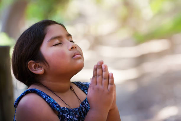 A young girl praying with hands together in reverence to God, wearing conservative clothing and in an outdoor setting.  prayer request stock pictures, royalty-free photos & images