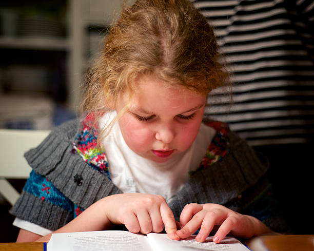 A young girl reading a book with her finger on page stock photo