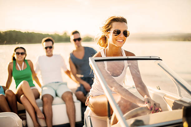 Young girl riding a speedboat. Cheerful blonde riding a speedboat, three young people in the background sitting on the edge of the boat.    motorboat stock pictures, royalty-free photos & images