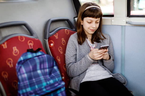 envoyer des sms sur le téléphone dans le bus jeune fille - smartphone car photos et images de collection