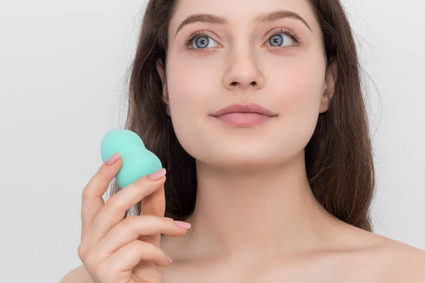 A young girl with a turquoise sponge for makeup. Looks up thoughtfully. A young girl with a turquoise sponge for makeup. Looks up thoughtfully. foundation stock pictures, royalty-free photos & images