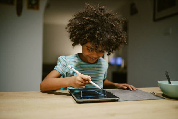 young girl writing on digital tablet at home after school stock photo