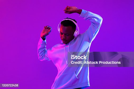 istock Young handsome African man wearing headphones listening to music and dancing in futuristic purple cyberpunk neon light background 1320722438
