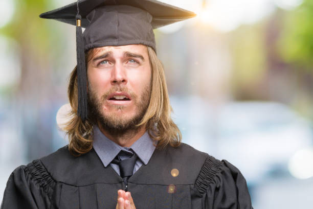 Young handsome graduated man with long hair over isolated background begging and praying with hands together with hope expression on face very emotional and worried. Asking for forgiveness. Religion concept.  prayer request stock pictures, royalty-free photos & images