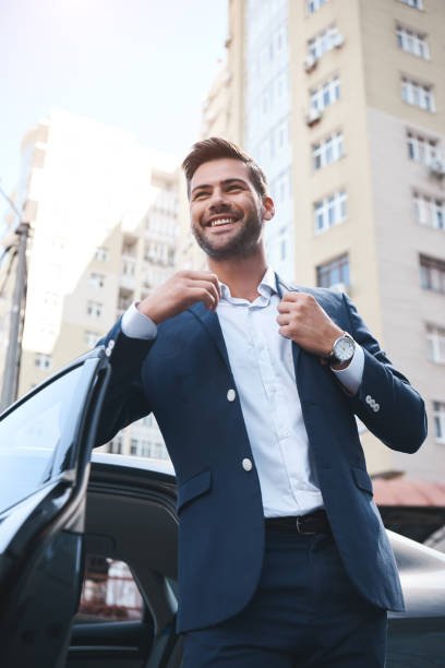 A young handsome man in a suit comes out of the car and laughs  man driving suit stock pictures, royalty-free photos & images