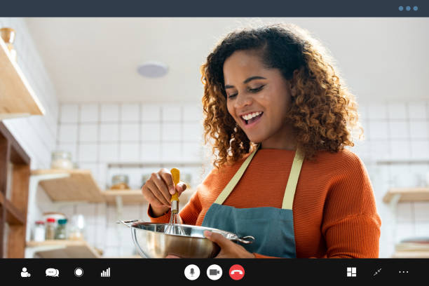Young happy African American woman making video call while cooking in kitchen at home during spare time stock photo