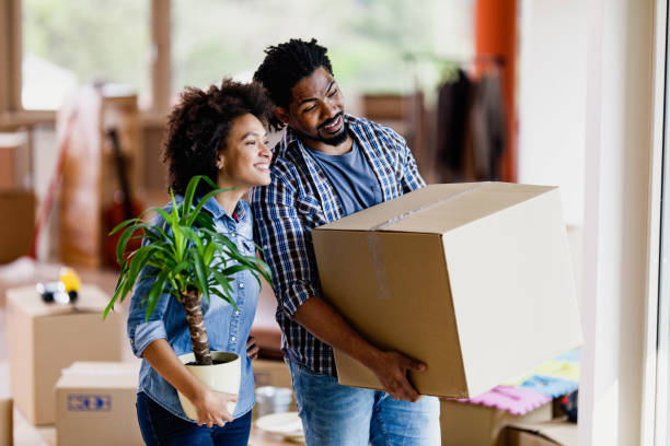 Young happy black couple relocating into new home. Happy African American couple moving into new apartment and looking through window. Focus is on man. unpacking stock pictures, royalty-free photos & images