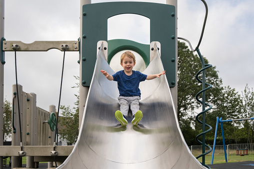 Close up of a young happy boy 2.5 years old at the top of a slide in an outdoor play park. England, UK.