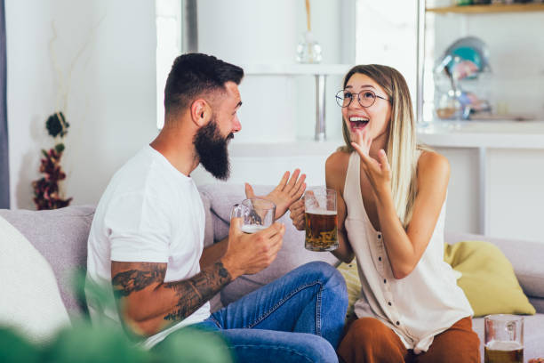 Young happy couple communicating while sitting on the sofa and drinking beer stock photo