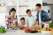 Young happy family making sandwich at home. Mom and dad preparing breakfast with sons.