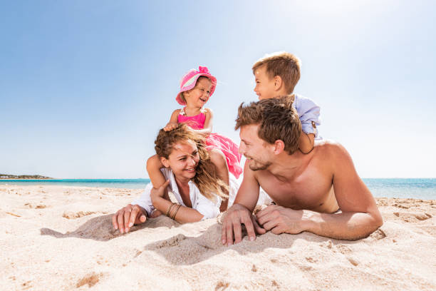 Young happy family talking while relaxing in sand on the beach. stock photo