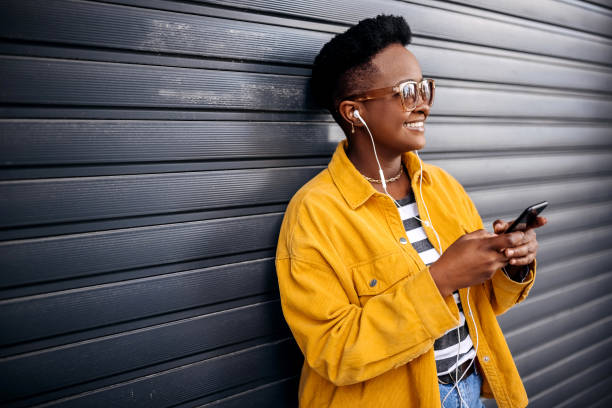 Young happy hipster girl posing with a mobile phone and earphones in front of black background stock photo