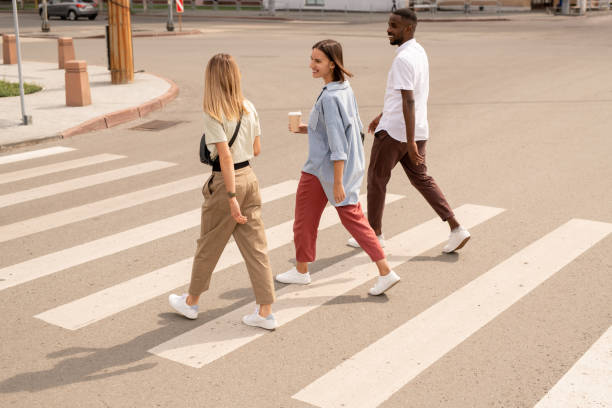 Young happy intercultural friends having drinks and talking while crossing road stock photo