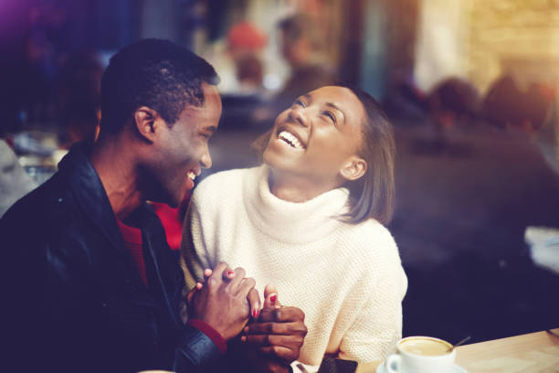 Young happy man and woman laughing together while sitting in modern restaurant during coffee break, cheerful couple in love with smiles on faces enjoying rest and good day while relaxing in bar stock photo